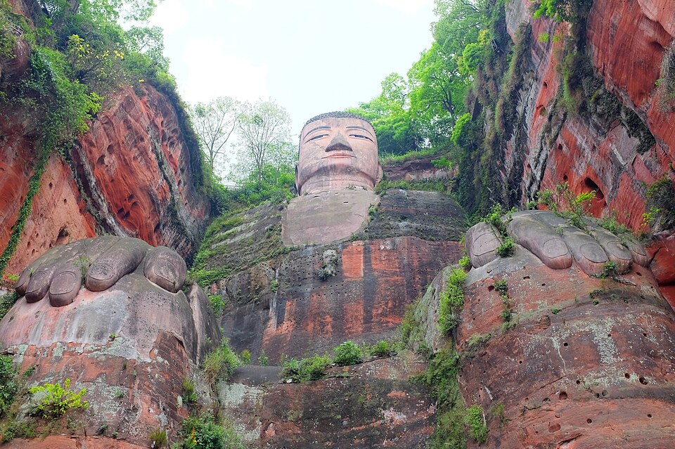乐山大佛的彩色仰视照片，可见佛像坐姿与岩壁背景